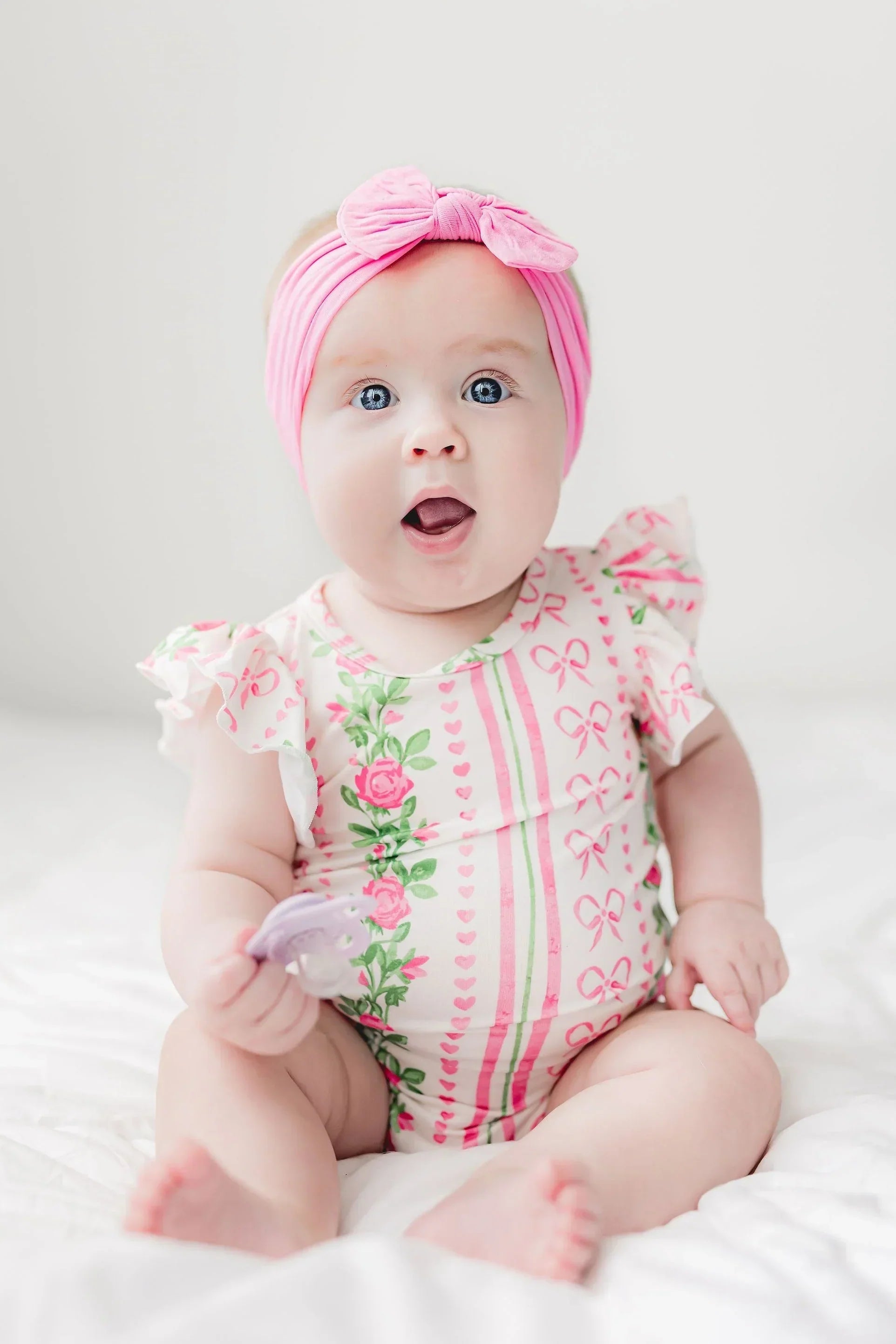 Baby wearing a floral and bow-print romper with a matching bright pink bow headband.