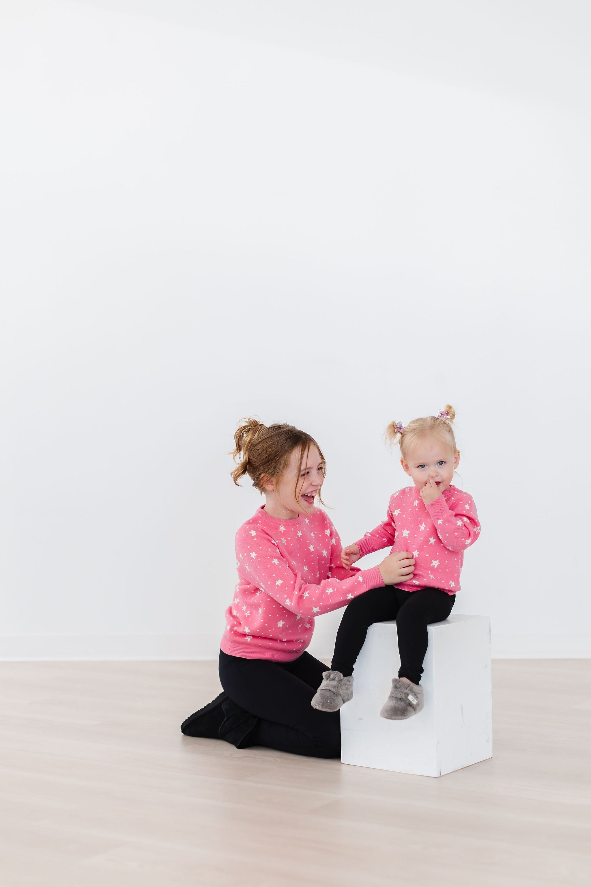 Two girls wearing matching pink star-patterned sweaters and black leggings, layered for winter comfort.