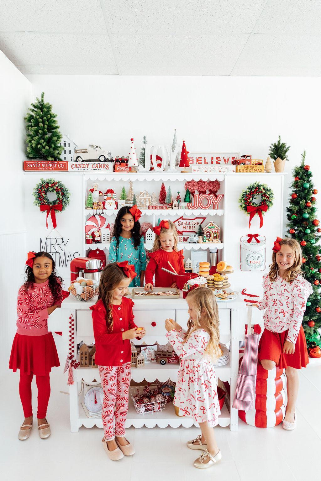 group of girls in various Christmas outfits in front of a kitchen set that is decorated for the Holidays