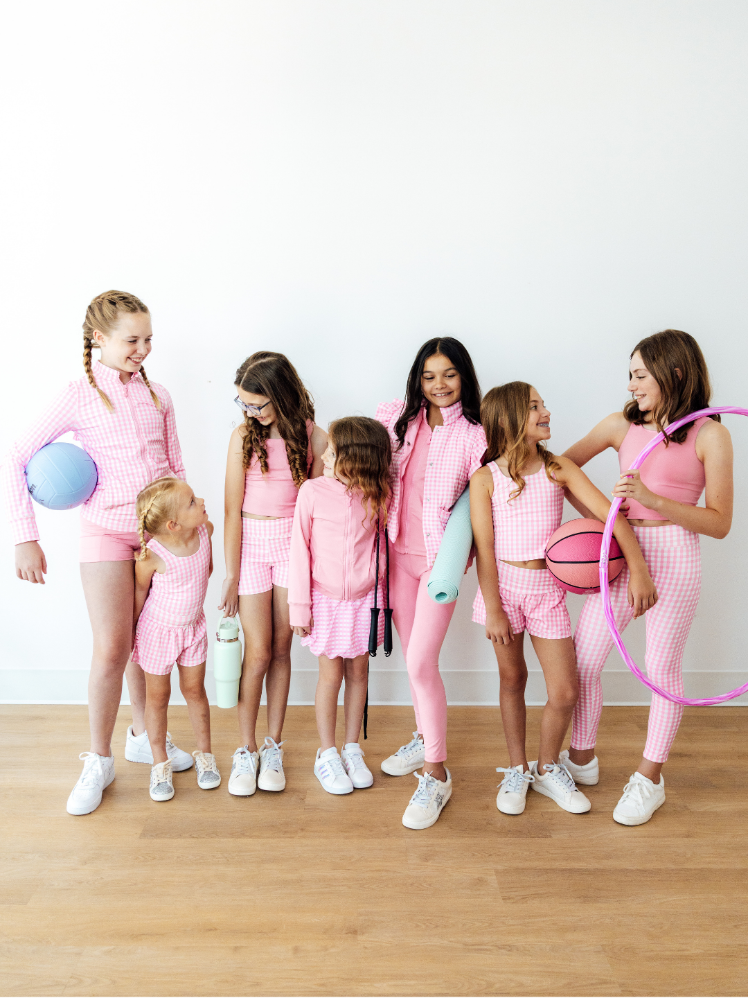 Group of girls wearing matching pink gingham activewear sets with sports gear.