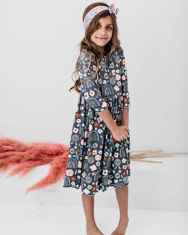 Girl wearing a dark grey floral and rainbow print dress with a matching headband for back to school.