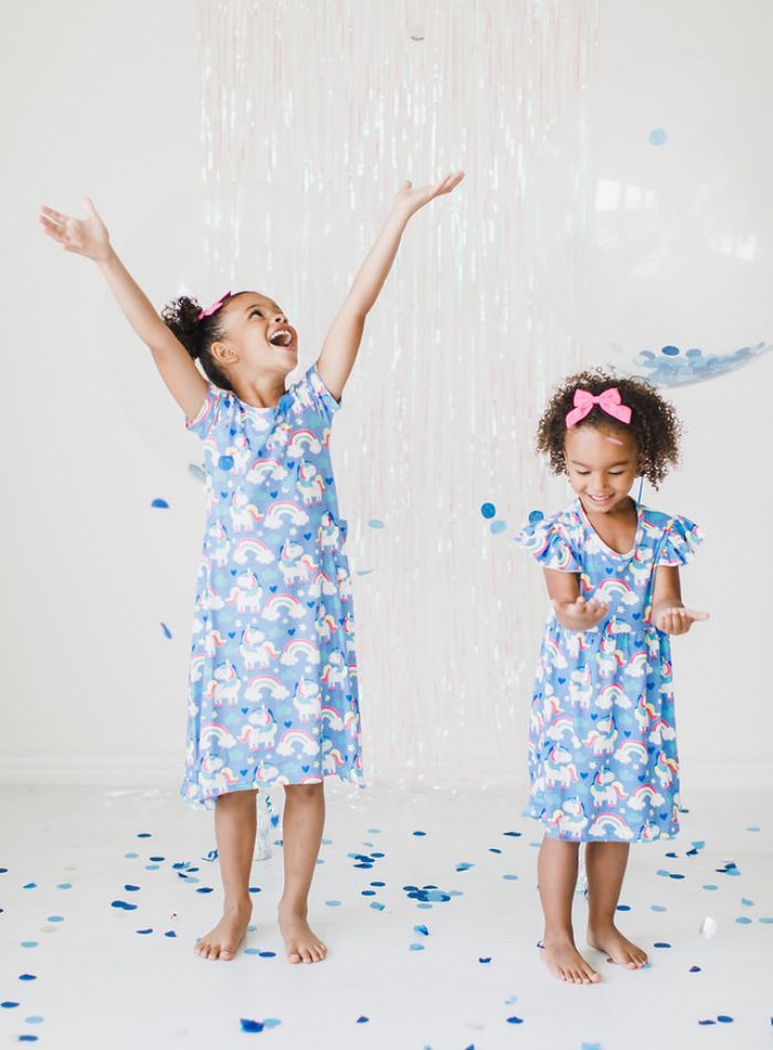 Two young girls in unicorn dresses celebrate New Year's Eve surrounded by blue confetti and a clear balloon.