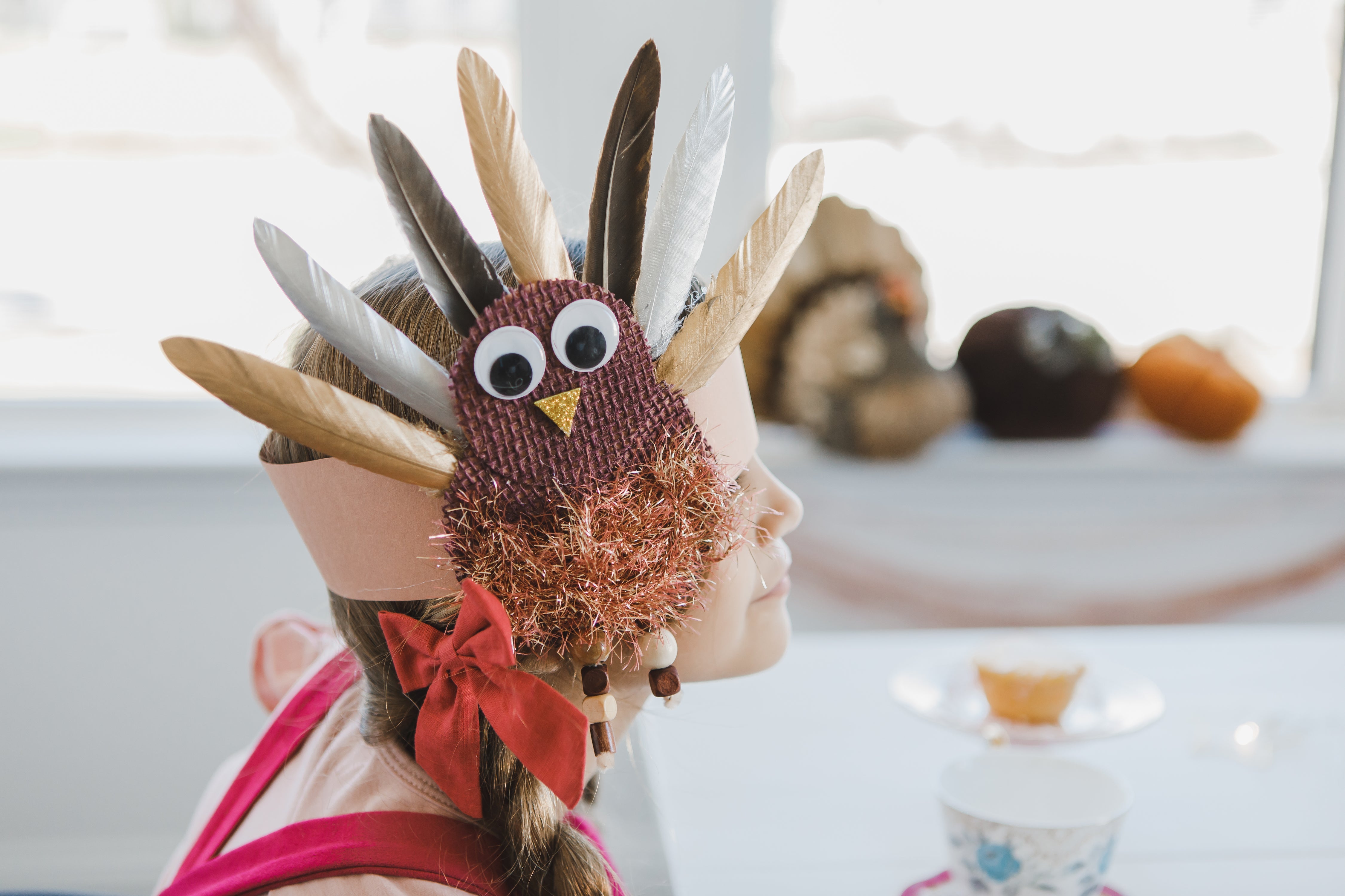Child wearing a DIY turkey headband made with brown burlap, googly eyes, and colorful feathers.