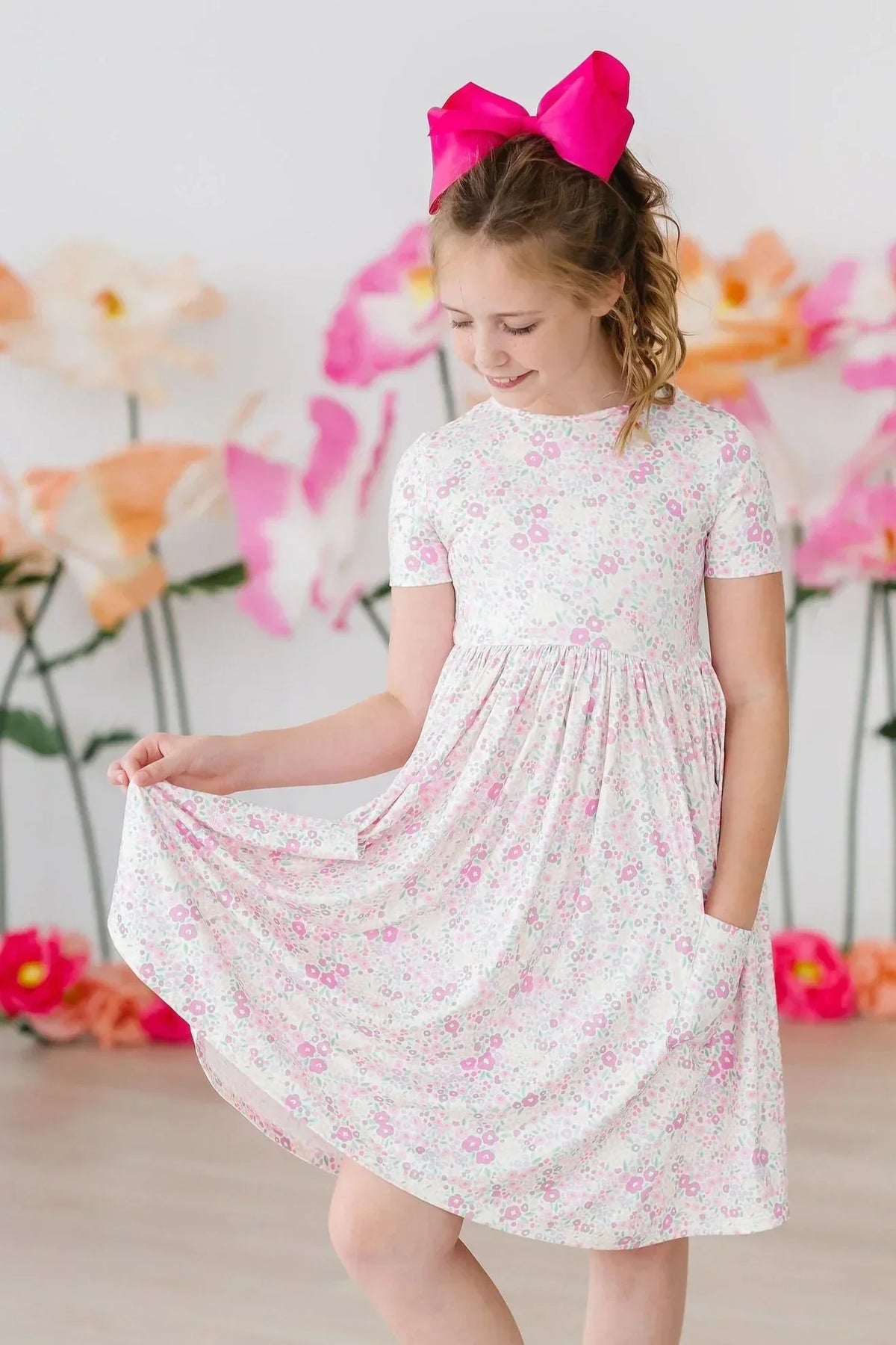 Girl wearing a pink floral dress with side pockets, holding up the skirt to show the placement.