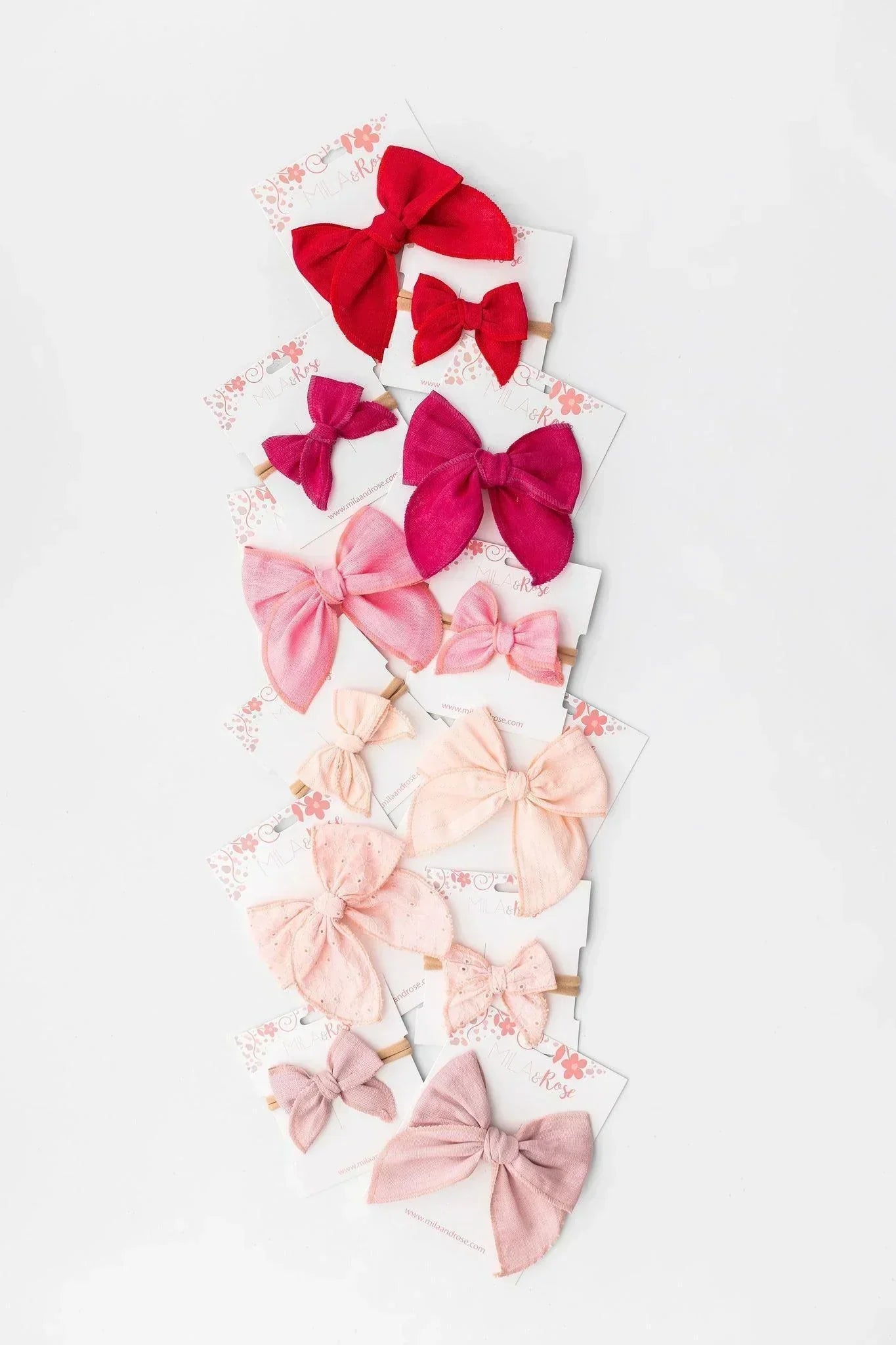 Assorted girls' hair bows in a gradient of pink and red shades, displayed on branded white display cards.