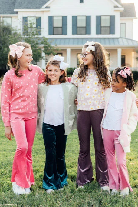 Four girls wearing cozy sweaters, velvet flare pants, and hair bows standing outside in a grassy yard.