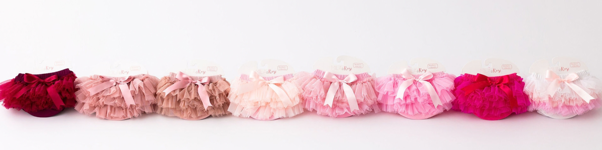 A row of fluffy newborn tutu bloomers in a gradient of pink, red, and white shades with satin ribbon bows.