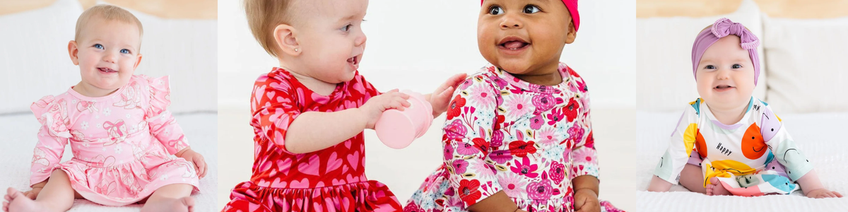 Happy babies wearing colorful, patterned long-sleeve dresses and a headband in a bright, cheerful studio setting.