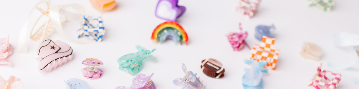 Assorted colorful acrylic hair claw clips in playful shapes like rainbows, cowboy hats, and checkered patterns.