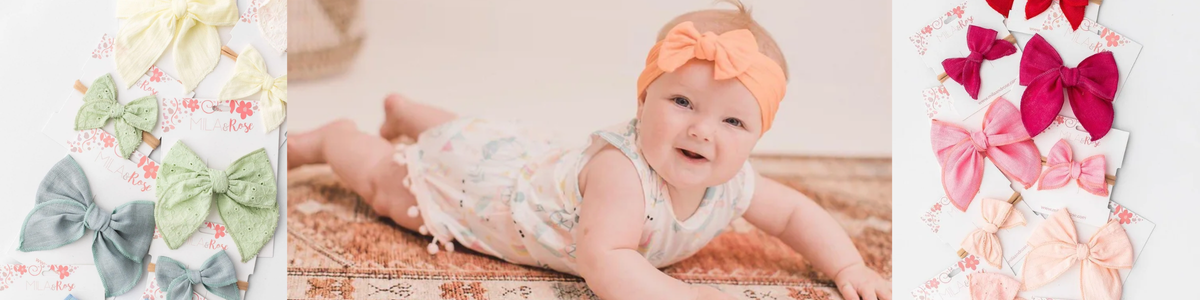 Baby wearing a peach bow headband surrounded by a colorful collection of soft fabric hair bows and headbands.
