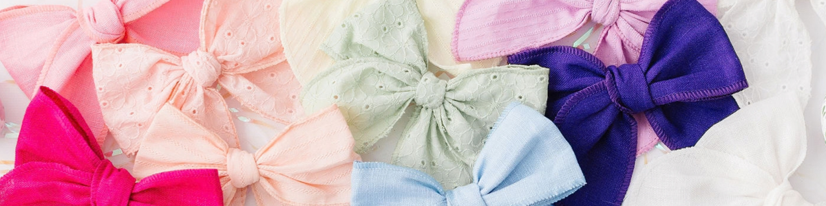 Assorted hand-tied hair bows in pastel and vibrant colors featuring textured eyelet and linen fabrics.