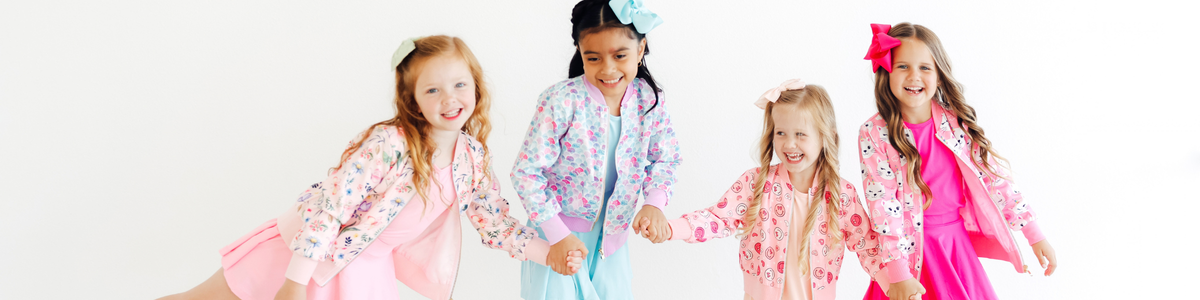 Four happy girls wearing colorful, patterned bomber jackets with matching hair bows against a white background.