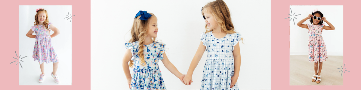 Young girls wearing colorful flutter sleeve twirl dresses with playful rainbow and fruit prints.