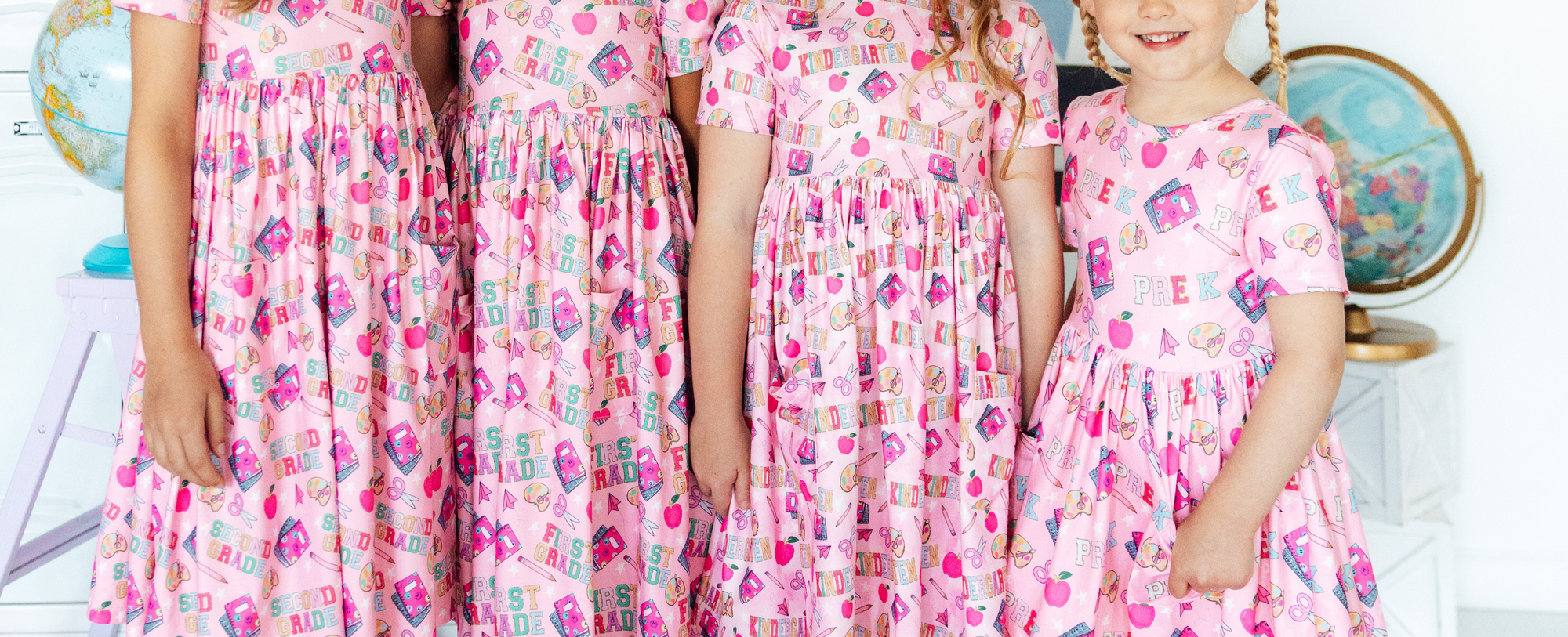 Group of girls wearing pink short-sleeve back-to-school dresses with colorful school supply and grade level patterns.