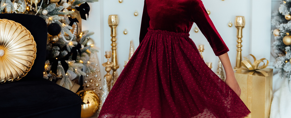 Girl wearing a festive deep red velvet tutu dress with a polka-dot tulle skirt in a holiday-decorated room.