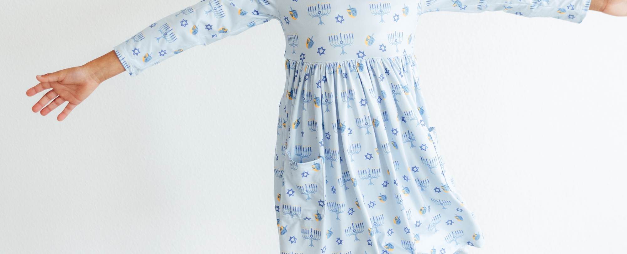 Light blue girls' Hanukkah dress featuring a festive menorah, dreidel, and Star of David print with a gathered skirt.