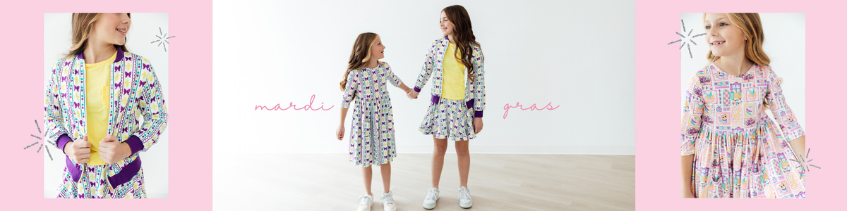 Two girls wearing matching white dresses and jackets with playful purple, yellow, and green Mardi Gras patterns.