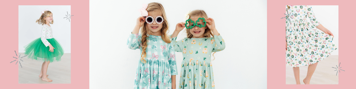 Two young girls in St. Patrick's Day dresses wearing festive daisy and shamrock-shaped sunglasses.