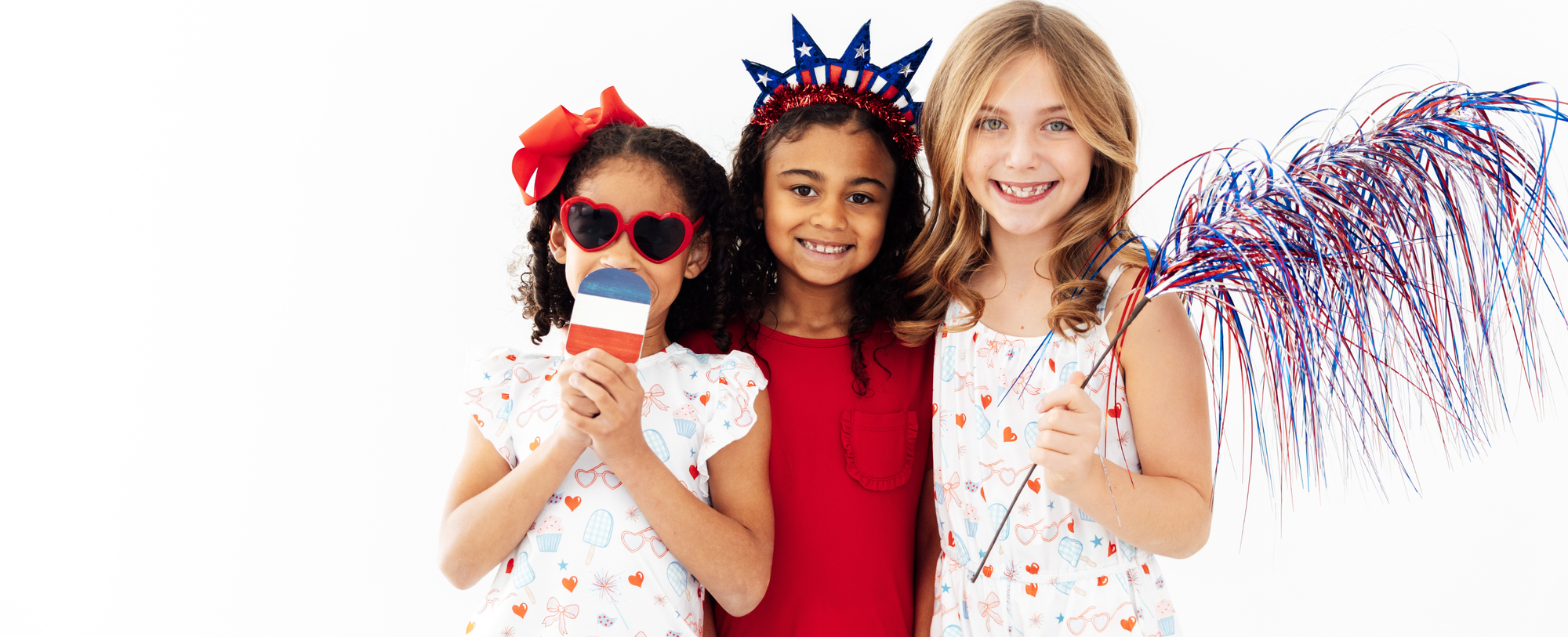 Three smiling girls in red, white, and blue 4th of July outfits, accessories, and festive party decorations.