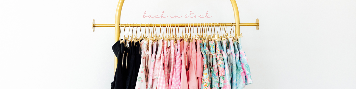 Gold clothing rack filled with a variety of colorful children's outfits in pink, floral, and black patterns.
