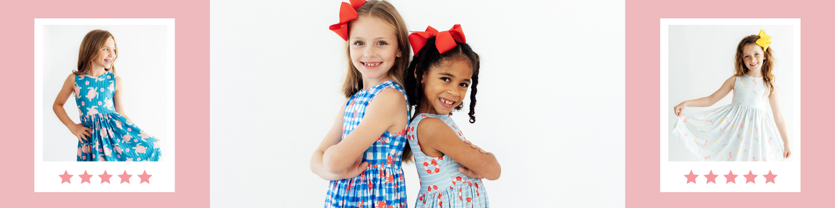 Two girls smiling in blue summer tank dresses with fun crab and life preserver prints, styled with bright hair bows.
