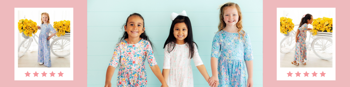 Three girls wearing colorful floral print wide leg jumpsuits standing against a light blue wooden wall.