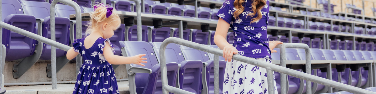 Two young girls wearing purple and white TCU Horned Frogs patterned outfits in a stadium with rows of purple seats.