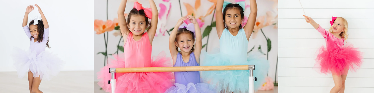 Young girls wearing colorful leotards with fluffy tulle tutus and matching hair bows in a playful ballet studio setting.