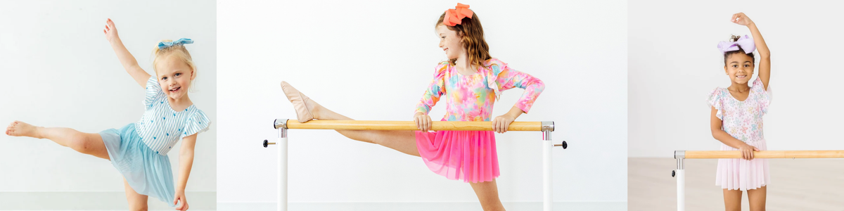 Young girls wearing colorful, ruffled twirl leotards while practicing ballet at a wooden barre.