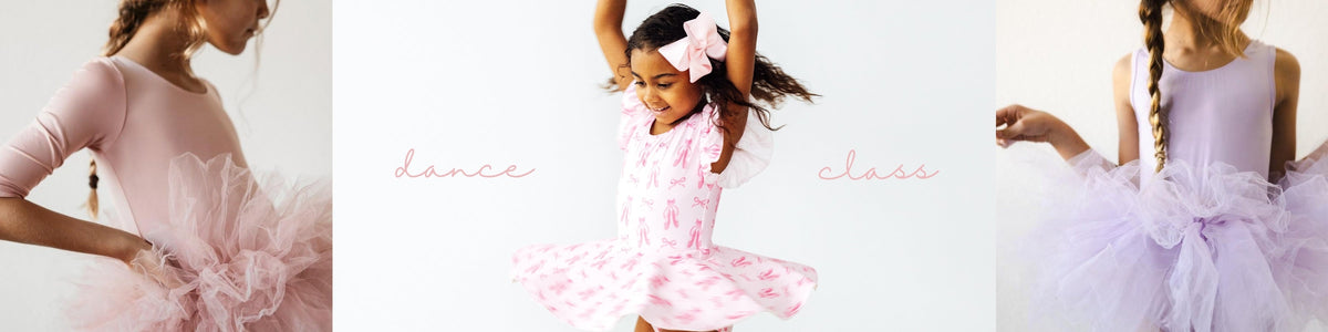 Young girl in a colorful tie-dye leotard and pink skirt practicing a leg stretch at a wooden ballet barre.